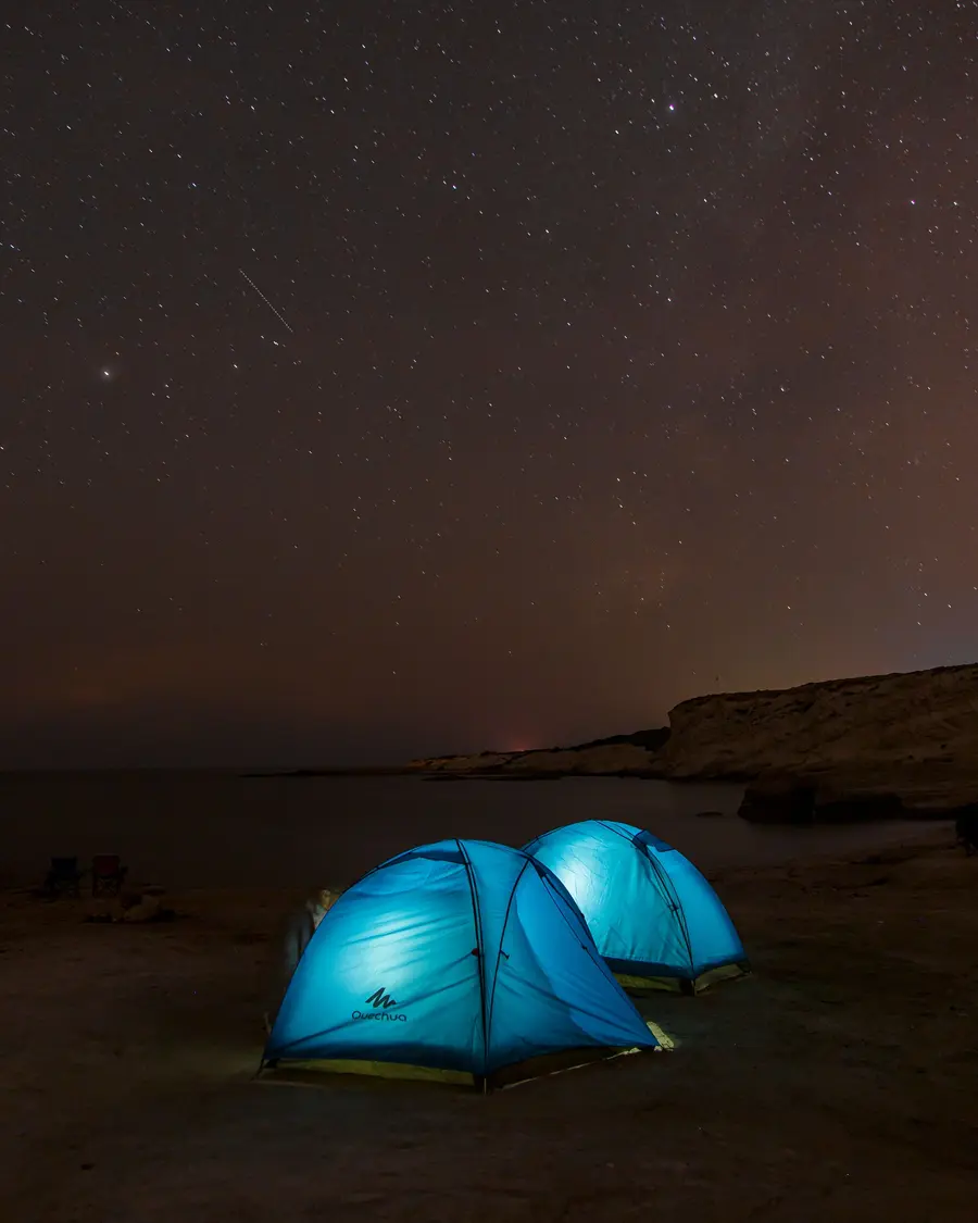 Duas barracas azuis iluminadas por dentro, sob um céu estrelado