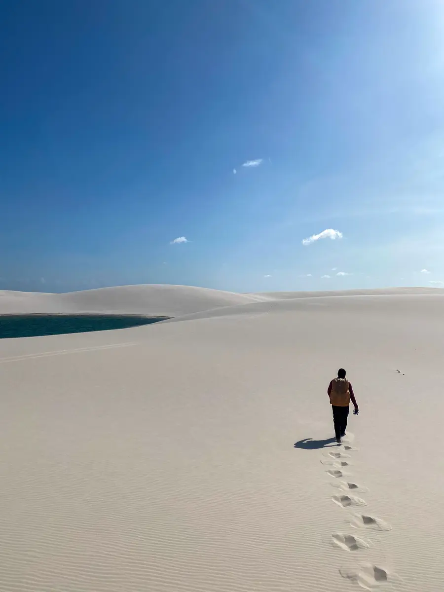 Pessoa caminhando nas dunas brancas em direção a uma lagoa azul