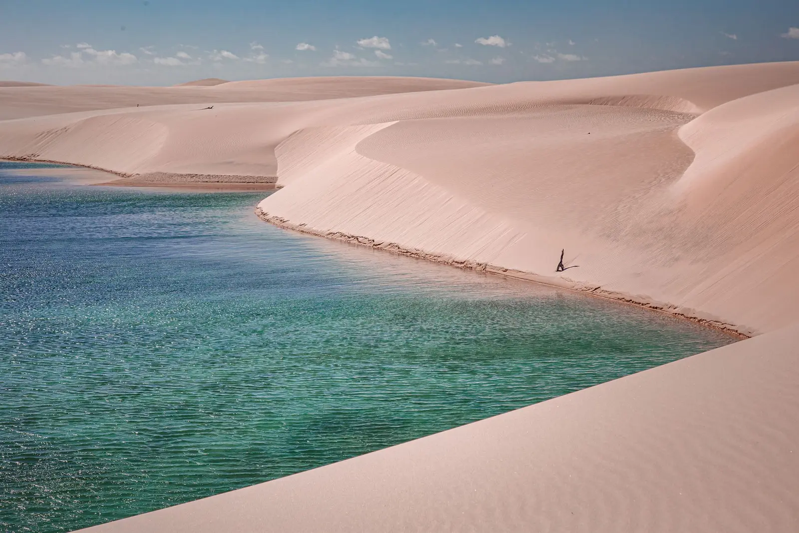 Lagoa verde-azulada entre dunas brancas, com uma pessoa pequena na margem