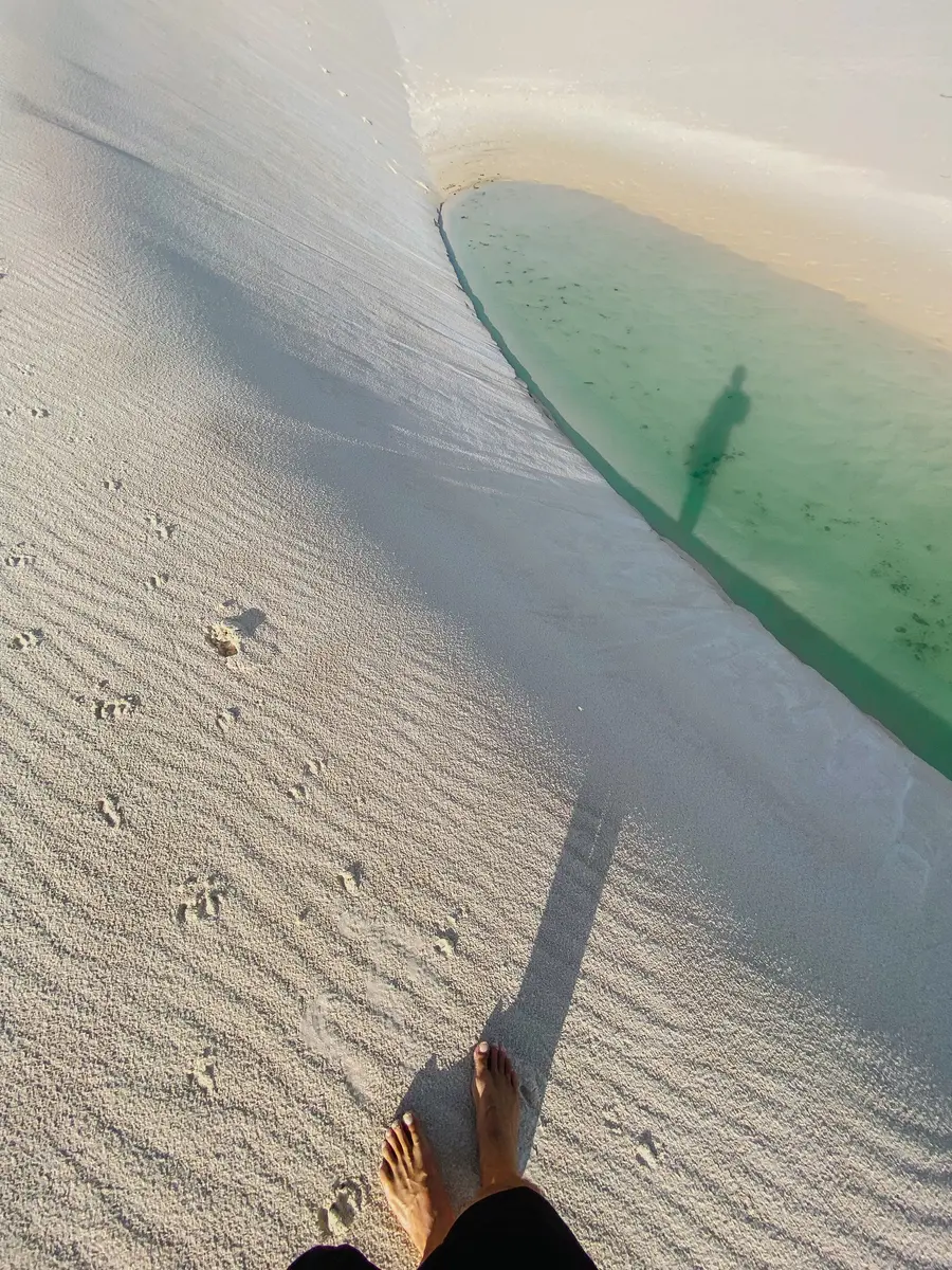 Pé descalço na areia branca, na beira de uma lagoa verde
