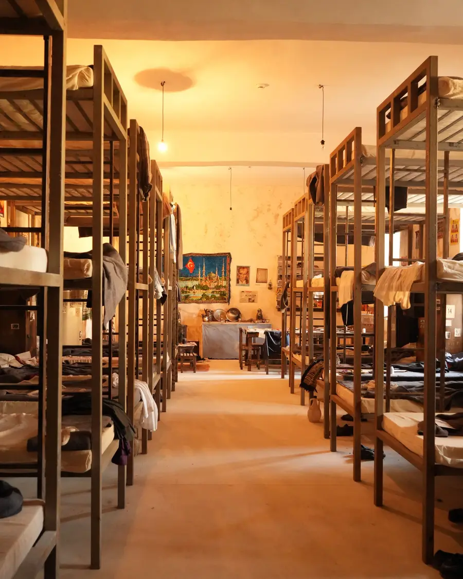 Quarto coletivo comprido, com beliches de madeira dos dois lados e luz amarela